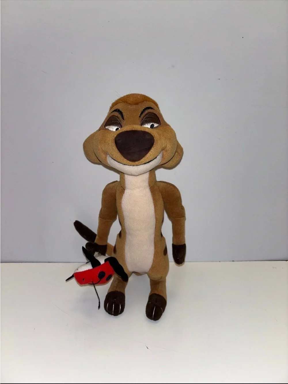 Disney The Lion King Timon plush toy holding a small red ladybug